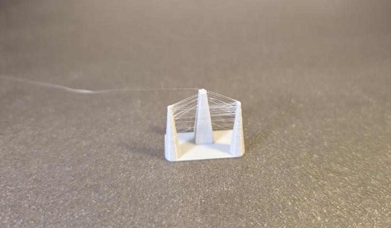 Ein Retraction-Test aus grauem Extrudr PETG mit starker Fadenbildung (Stringing) zwischen den kleinen Türmchen.